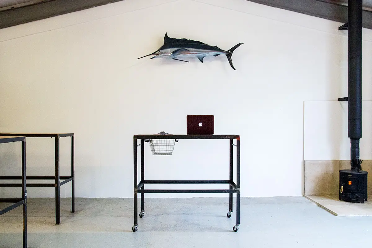 a standing desk at the hailer creative content studio in st agnes, cornwall, with a marlin on the wall above it and a woodburning stove in the corner of the room